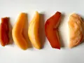 Cinq morceaux de fruit coing cuit, allant du rouge profond à l'orange clair, disposés en ligne sur fond blanc.