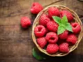 Un panier de framboises fraîches, garni de menthe, sur fond de bois. Idéal pour savoir comment conserver des framboises.