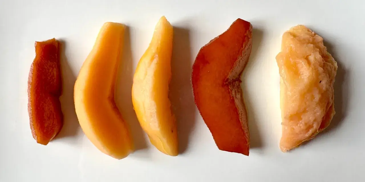 Cinq morceaux de fruit coing cuit, allant du rouge profond à l'orange clair, disposés en ligne sur fond blanc.